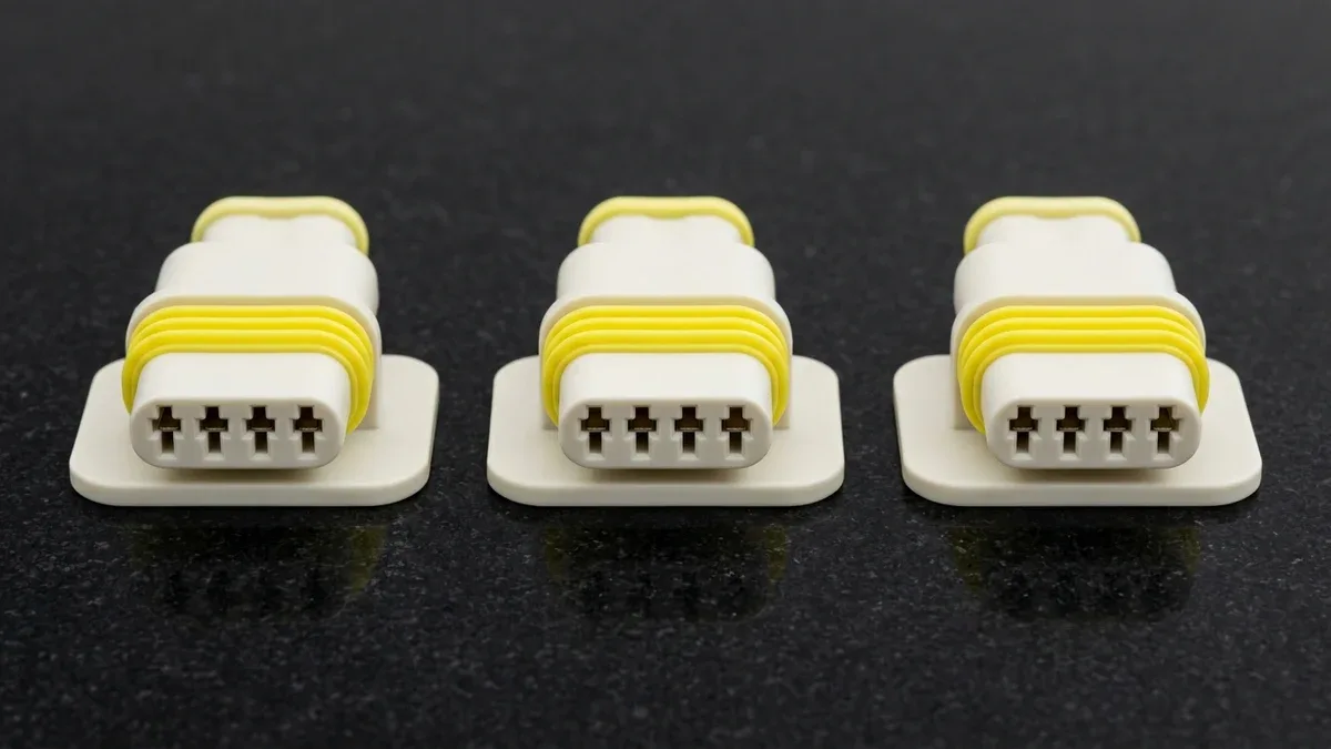 Three two-shot overmolded white PBT and yellow LSR waterproof automotive electrical connector housings on black granite