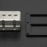 CNC-milled 316L stainless steel hydraulic manifold block beside a CNC-routed matte black PMMA acrylic instrument bezel