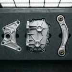 Side-by-side comparison on a granite surface plate of a CNC-milled 6061-T6 billet bracket, an A380 die-cast housing bracket, and a 7075-T6 forged suspension link