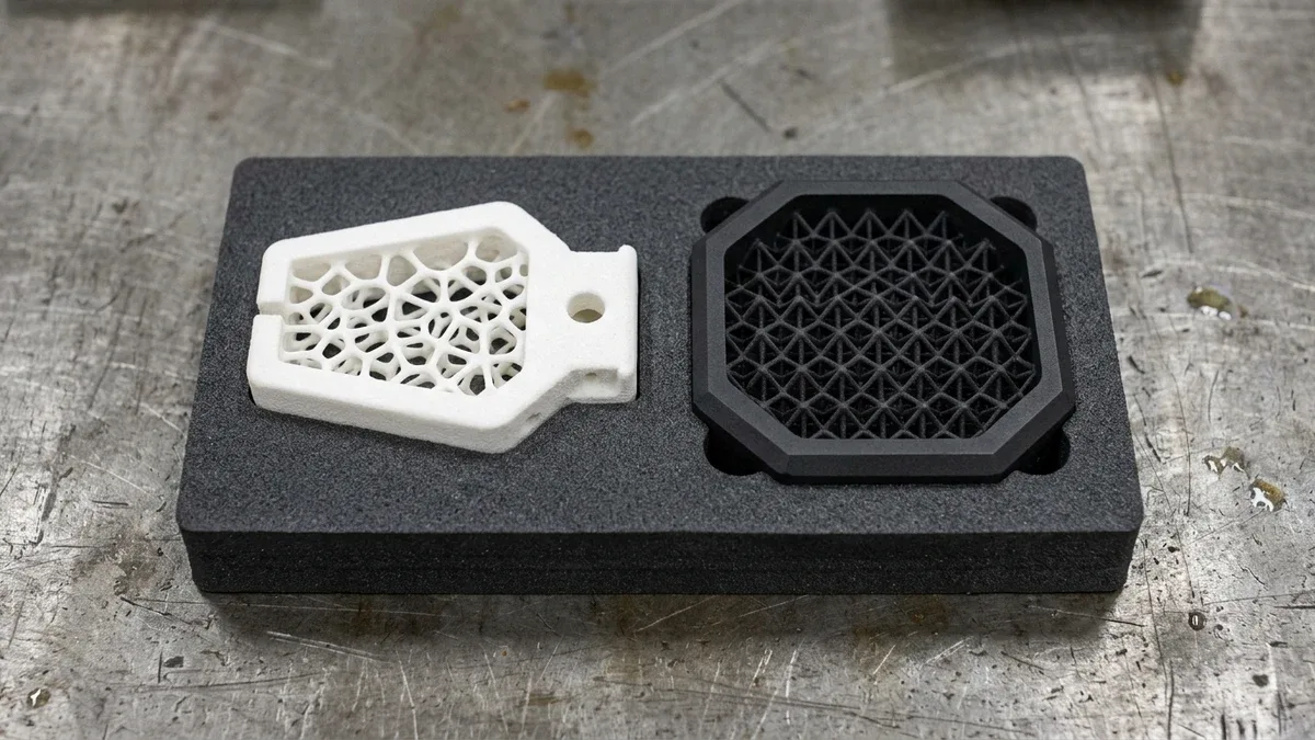 SLS white PA12 nylon Voronoi lattice robotic gripper finger beside an MJF black PA12 octet-truss mount