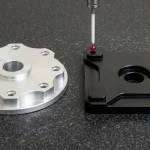 Clear-anodized 6061-T6 rotary flange and black 7075-T6 motor mount plate undergoing bridge CMM ruby probe inspection